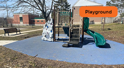 A play structure on top of blue colourful recycled rubber surfacing with buildings and a bench in the background.