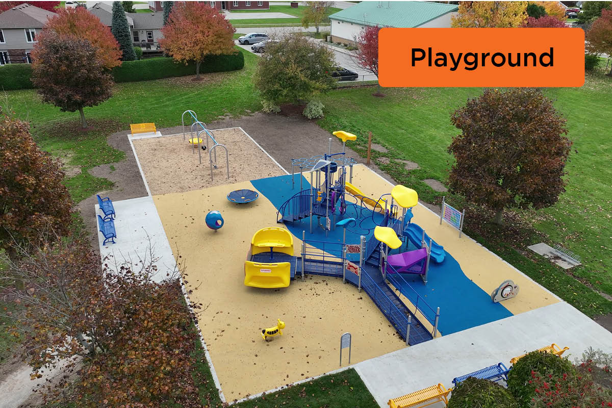 An aerial photo of a playground with a colourful rubber surface, ramps, and wheel chair accessible play equipment in a park.