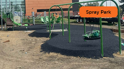 A playground in construction with a freshly pour-and-place rubber surface under green play equipment.