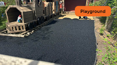 Pour-in-place black recycled rubber surfacing installation with a wooden train play structure.